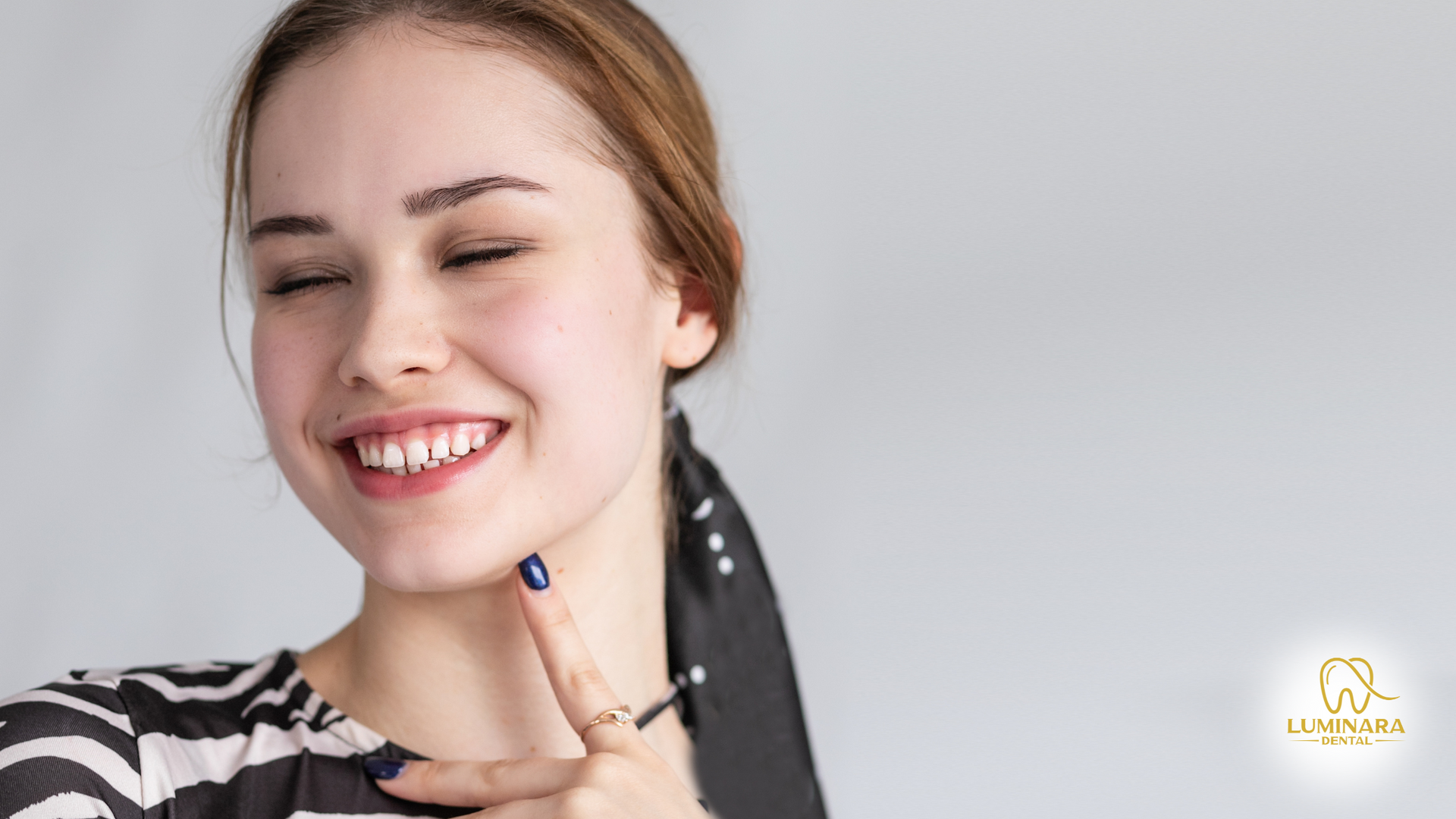 A woman is smiling with her eyes closed and her hand on her chin.