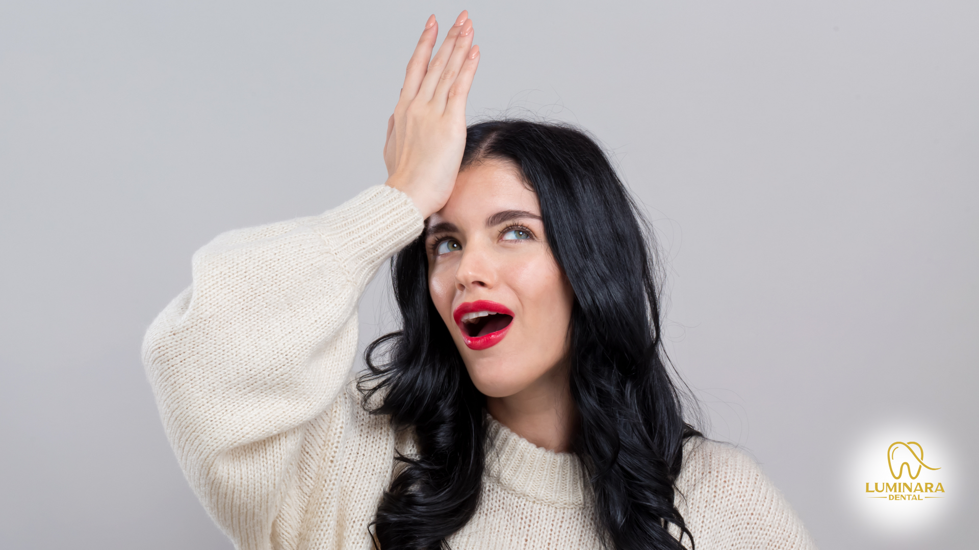 A woman in a white sweater is covering her face with her hand.