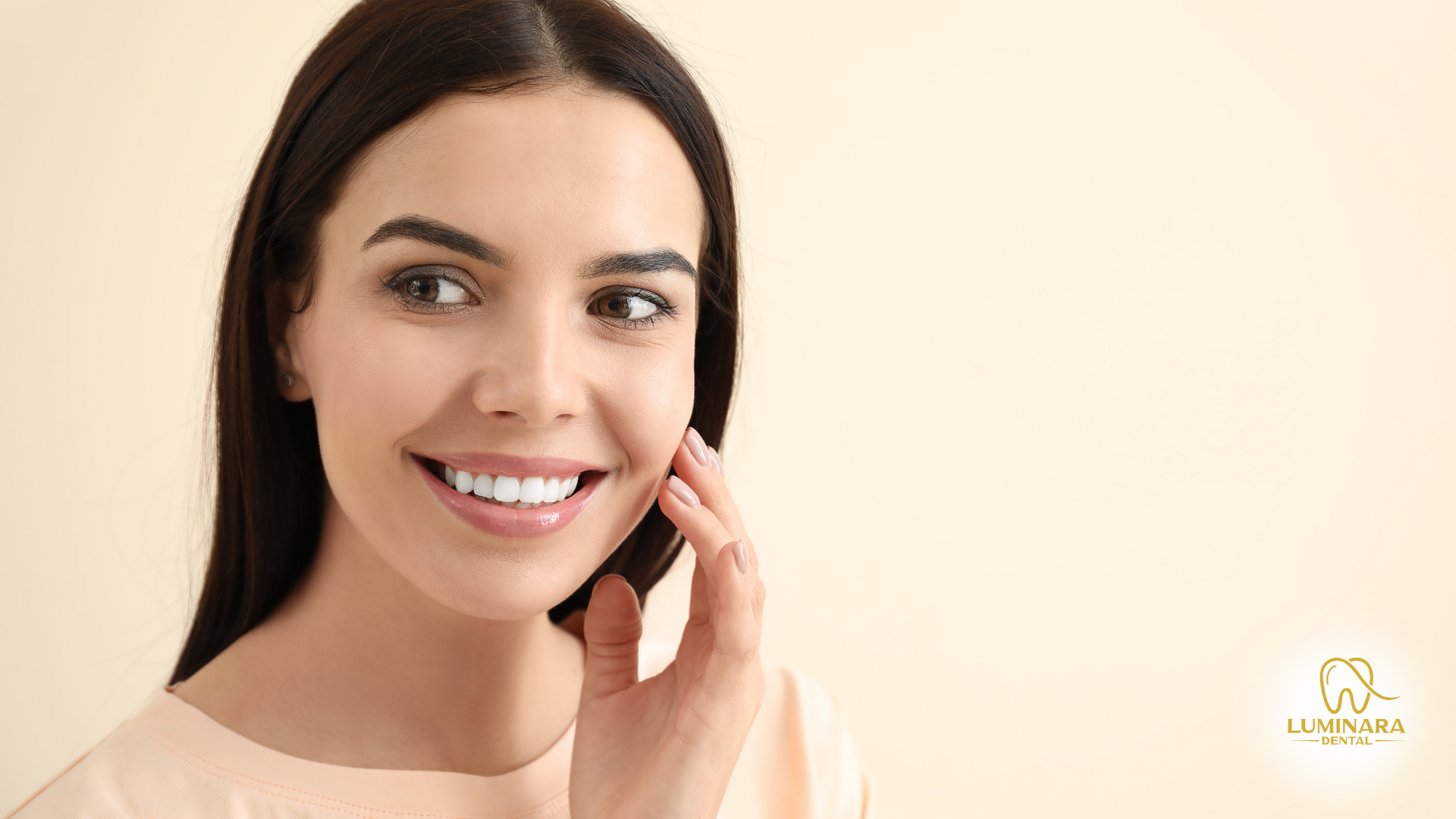 A woman is smiling and touching her face with her hand.