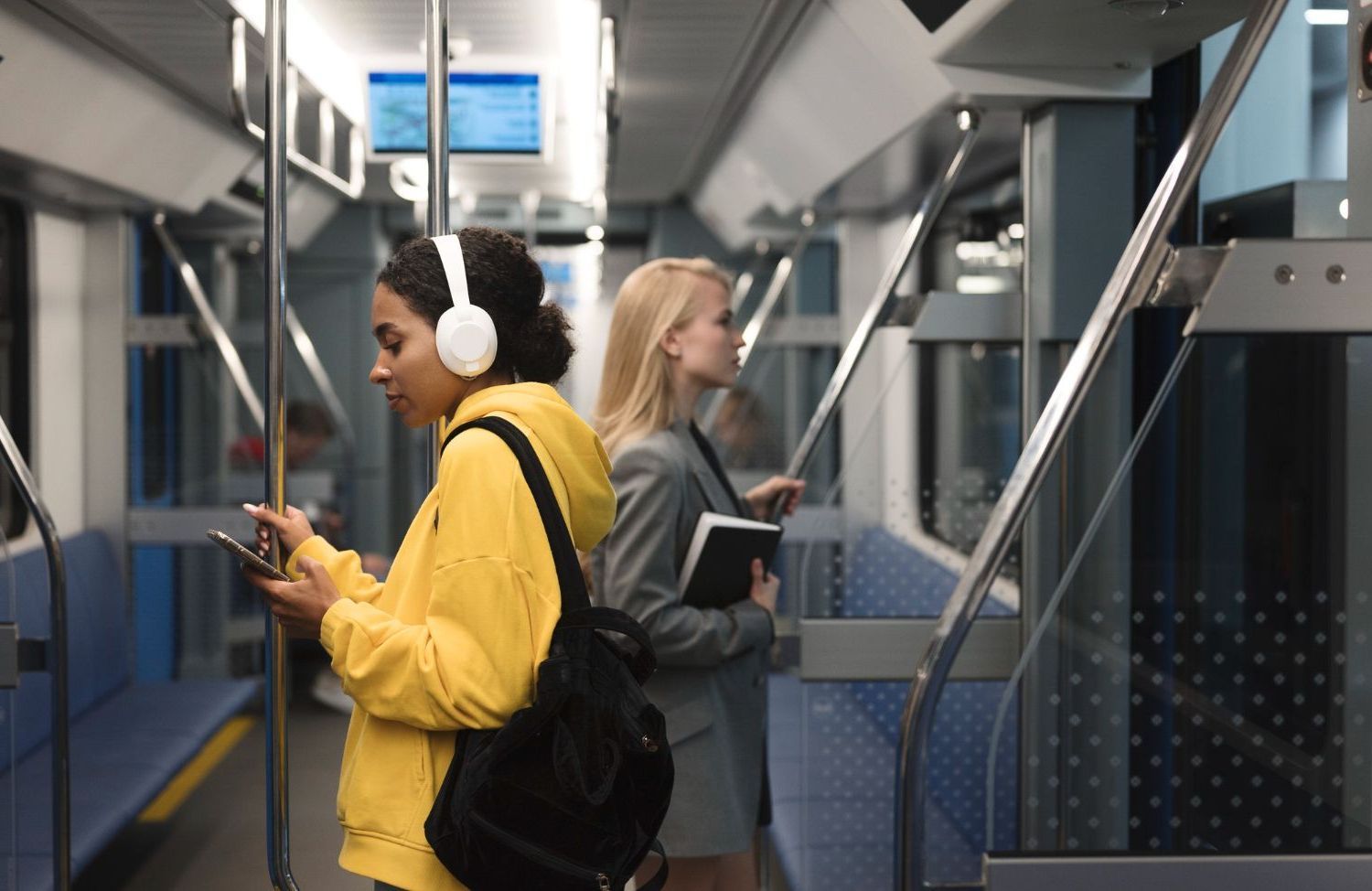 A woman wearing headphones is using a cell phone on a subway train.