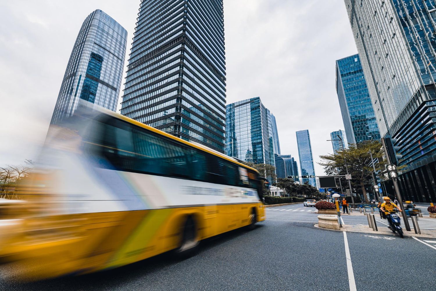 A yellow bus is driving down a city street in front of tall buildings.
