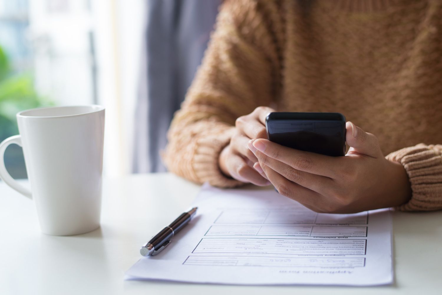 A person is sitting at a table using a cell phone.
