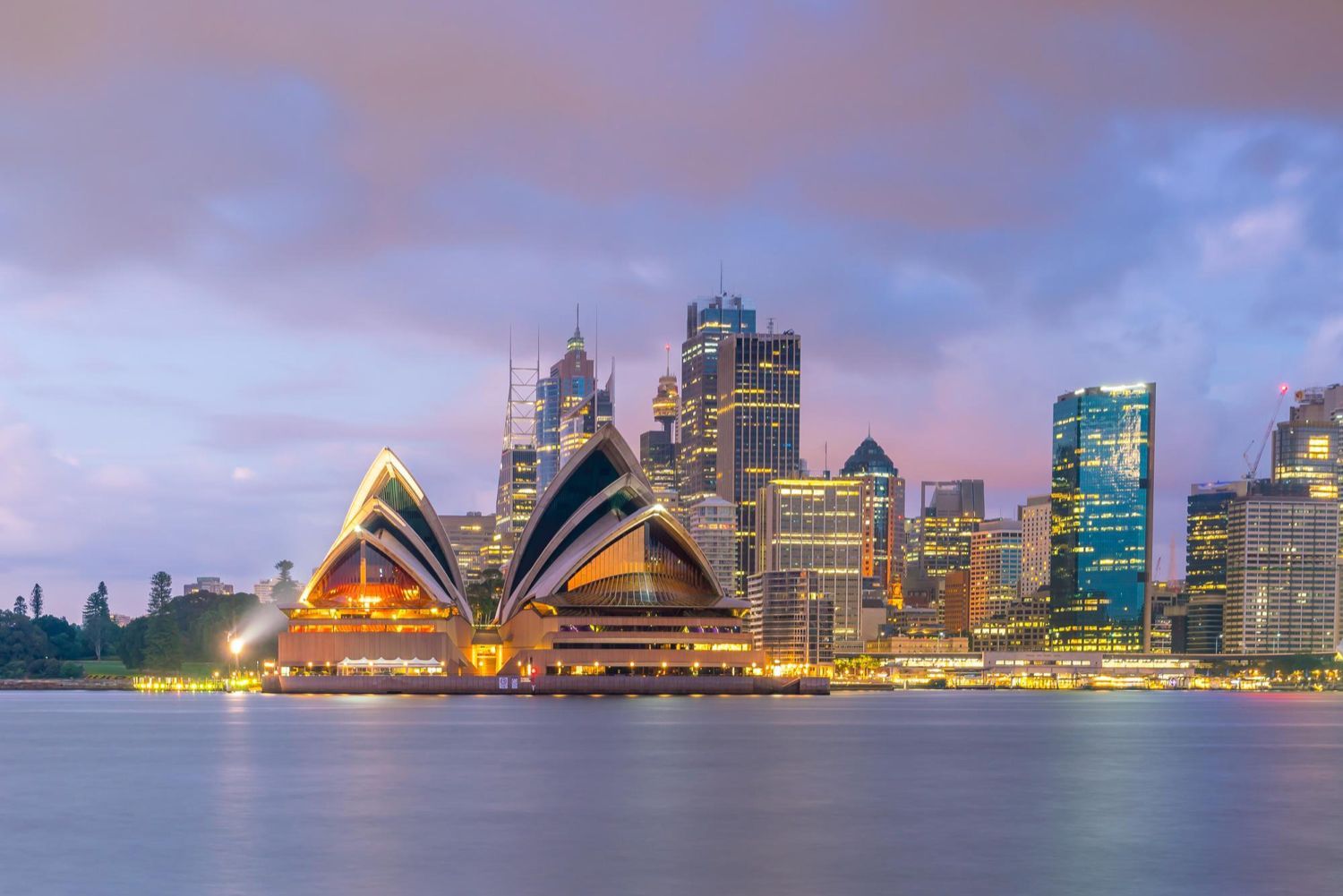 The sydney opera house is lit up at night with a city skyline in the background.