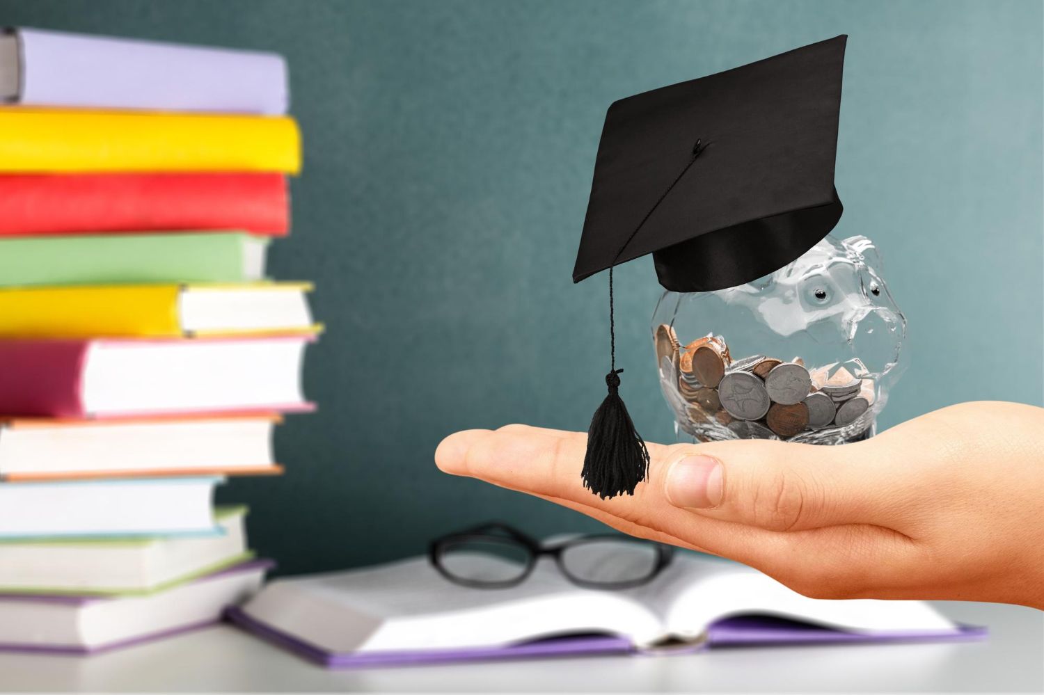 A hand holding a piggy bank with a graduation cap on it