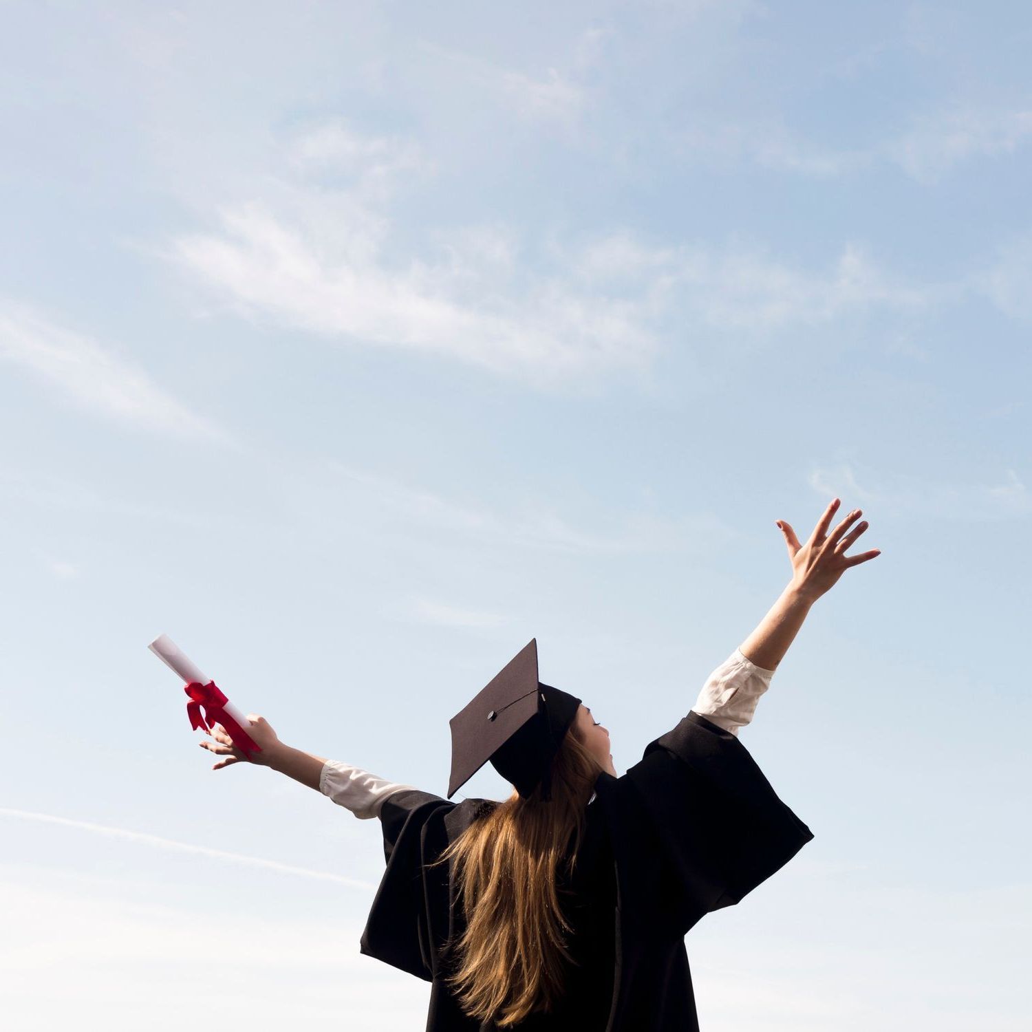 A woman in a graduation cap and gown is throwing her diploma in the air