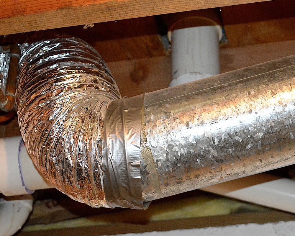 A metal pipe is connected to a white pipe under a wooden ceiling.