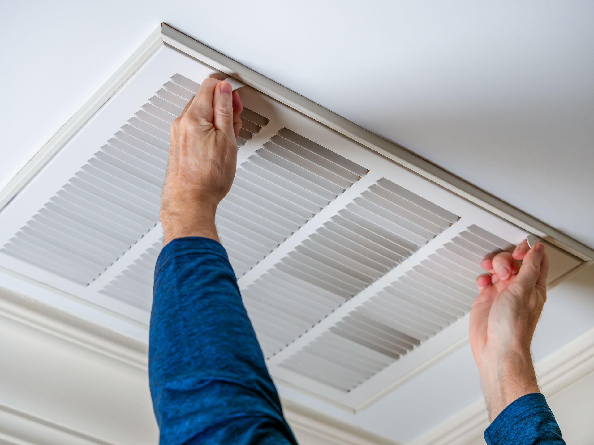 a person in a blue shirt is adjusting an air vent on the ceiling