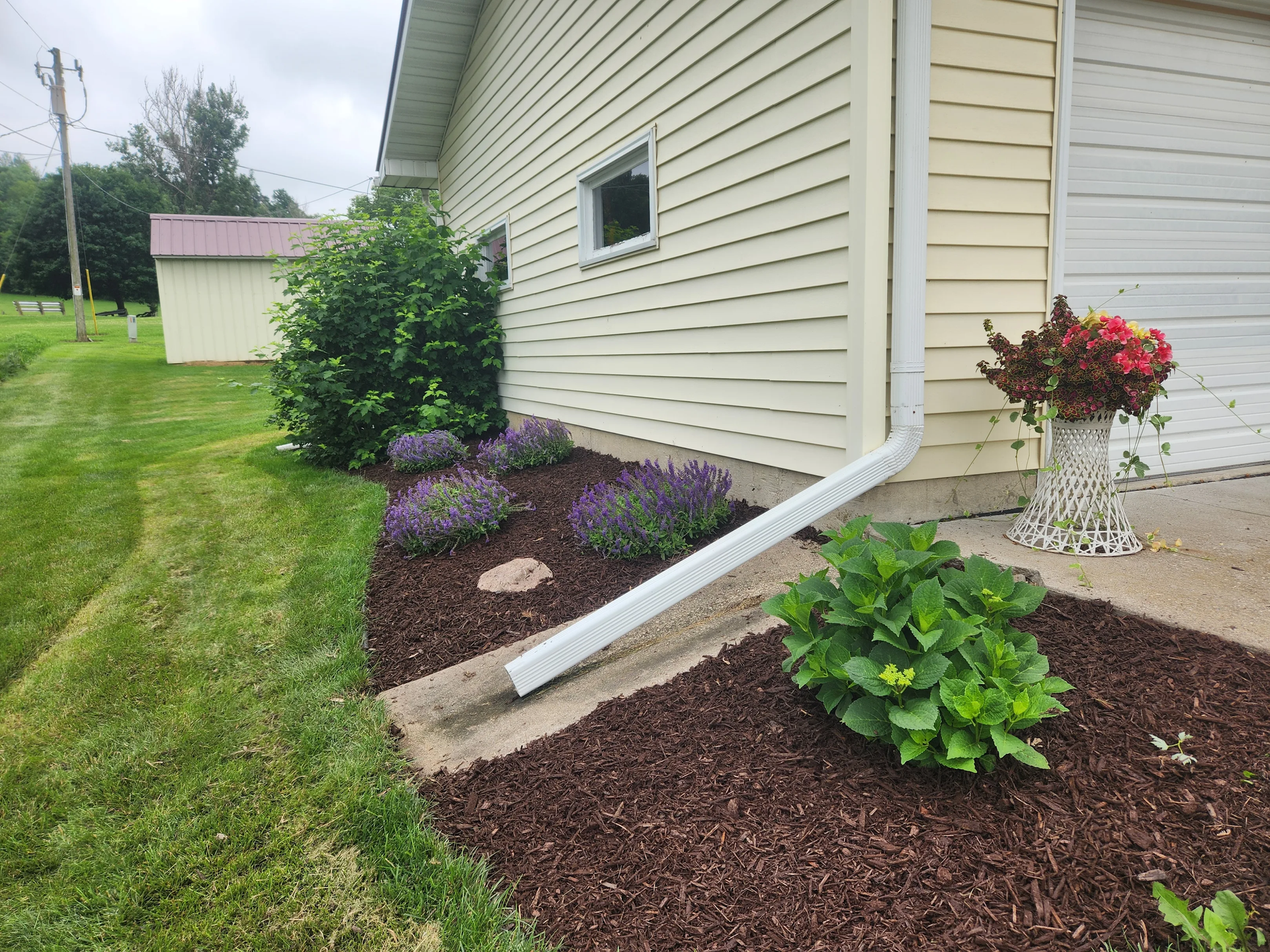 A house with a gutter on the side of it and flowers in front of it.