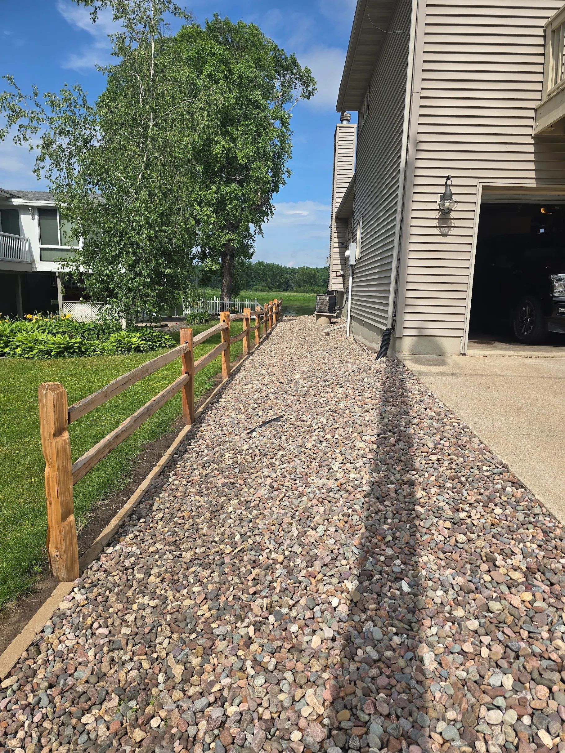 A gravel driveway leading to a house with a wooden fence.