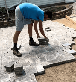 A man is laying bricks on a patio.