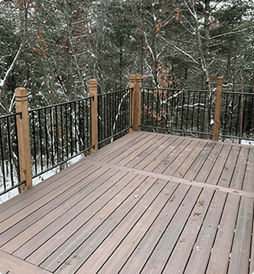 A wooden deck with a metal railing and trees in the background.