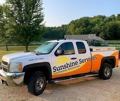 A white and orange sunshine services truck is parked in a gravel lot.