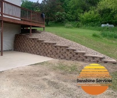 Retaining wall with steps leading up to a deck, built on a slope with gravel and grass.