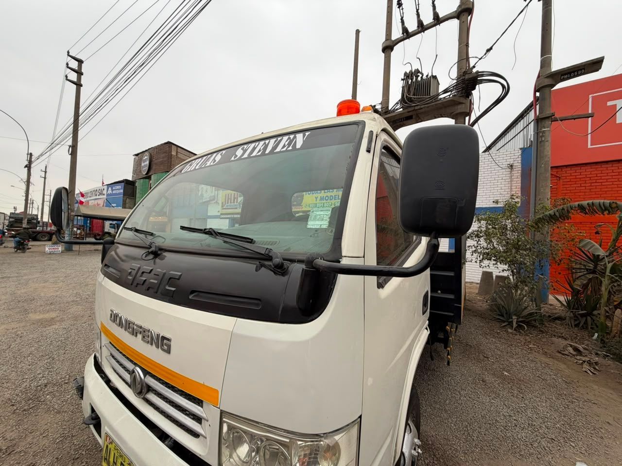 Camioneta blanca estacionada al costado de la carretera, debajo de líneas eléctricas, con una luz naranja en el techo.