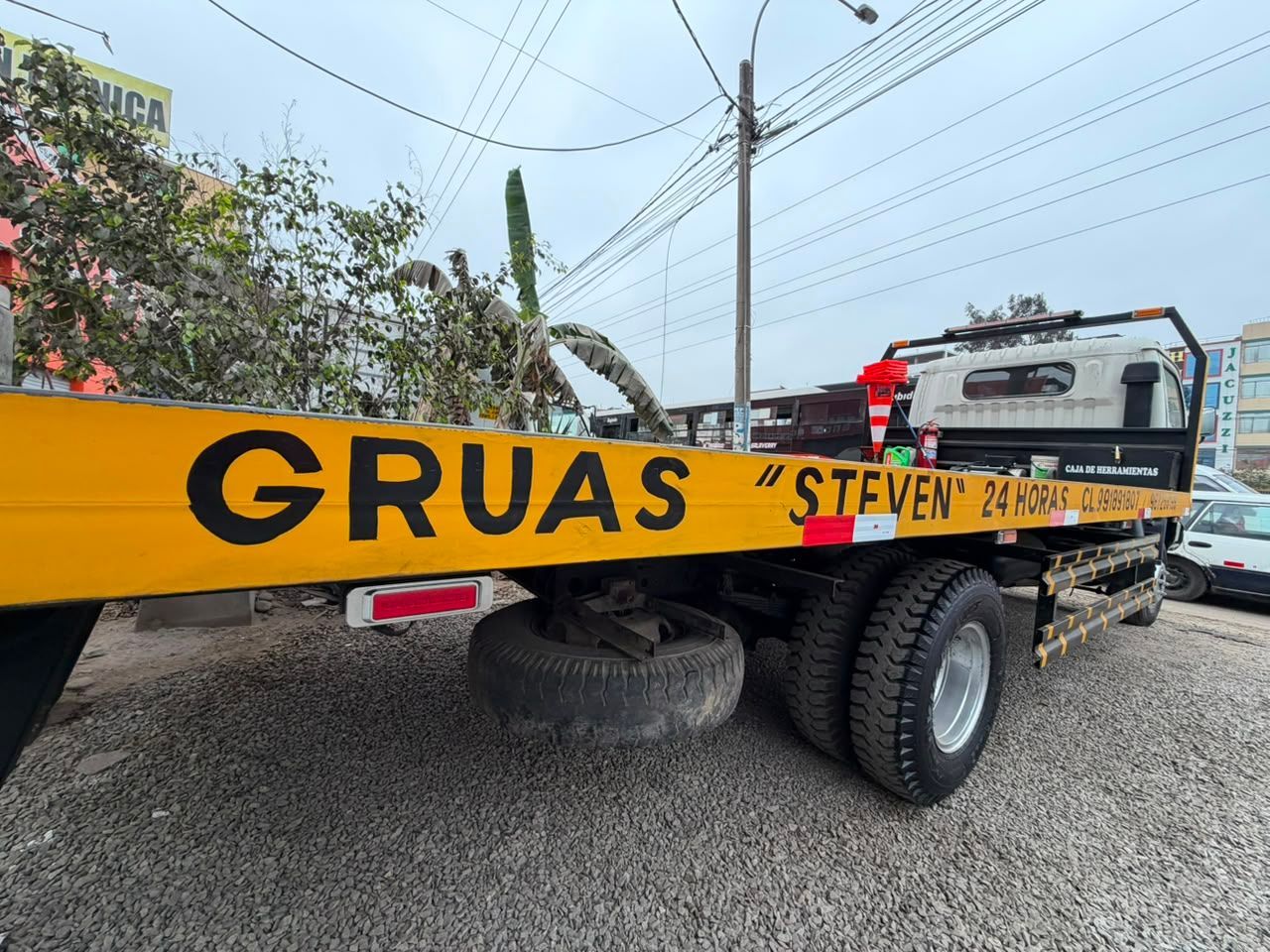 Grúa amarilla de GRUAS en camino de grava con plataforma y neumáticos grandes.