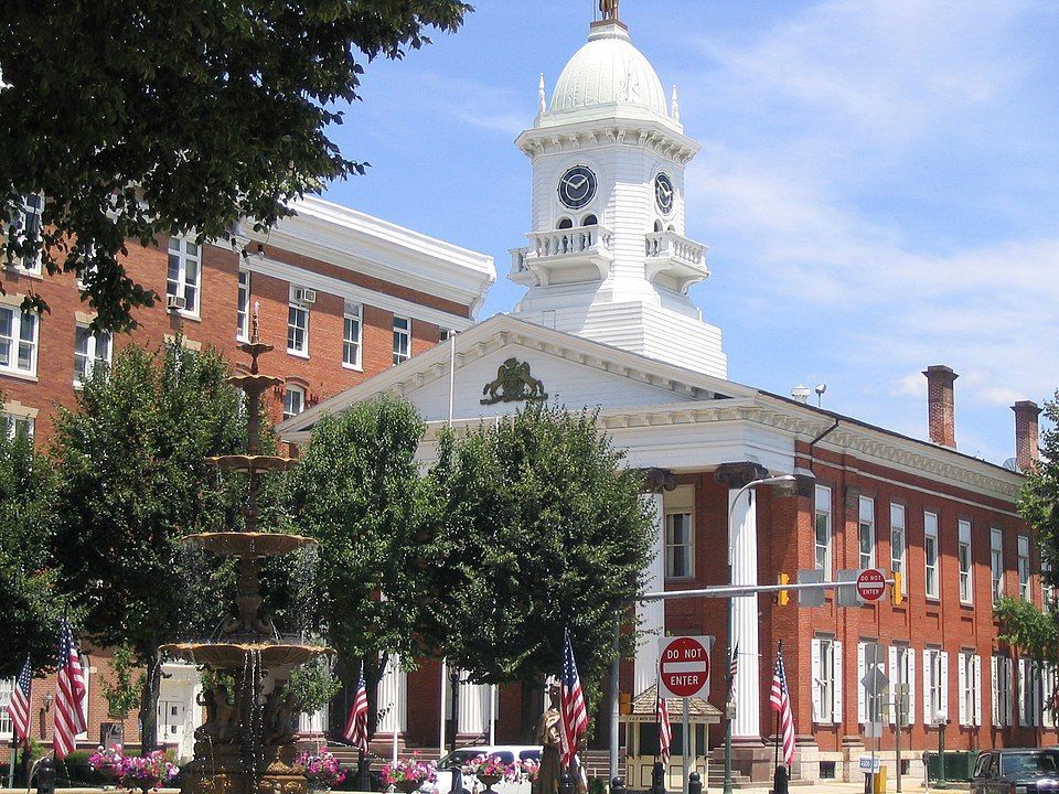 Brick courthouse with a white clock tower under a blue sky, flags and a fountain in foreground.