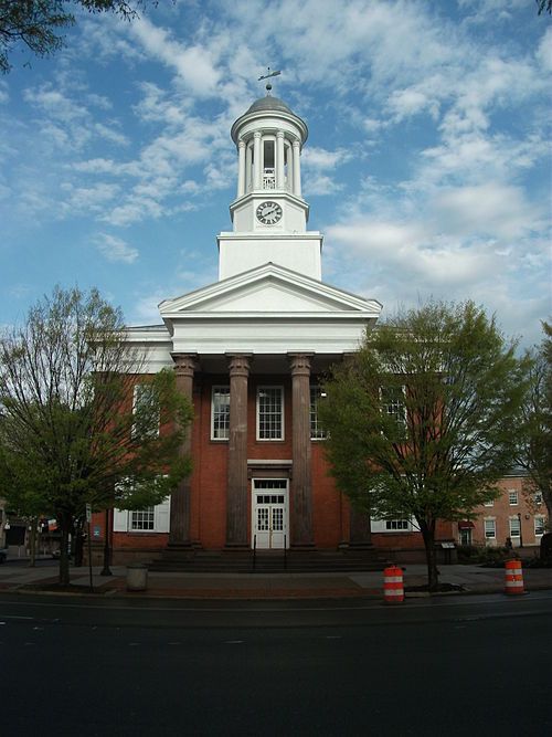 Brick courthouse with white columns, clock tower, and trees in front.