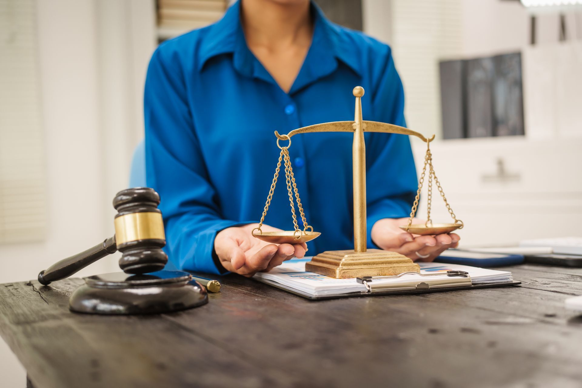 Person holding scales of justice, gavel on table, legal setting.
