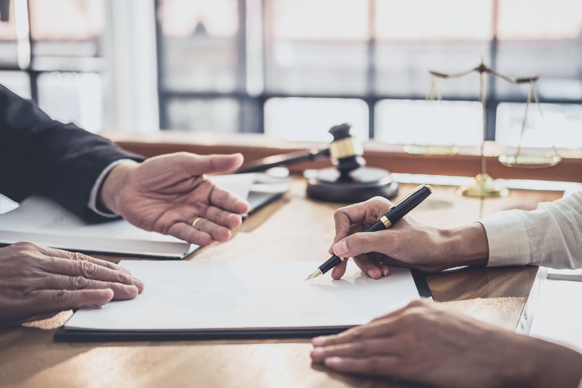 Hands signing a document on a desk, gavel and scales of justice in background.