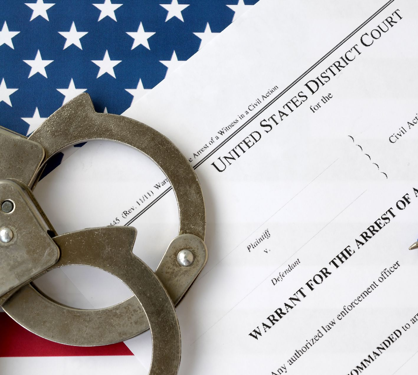 Handcuffs on a U.S. District Court warrant, with American flag in the background.