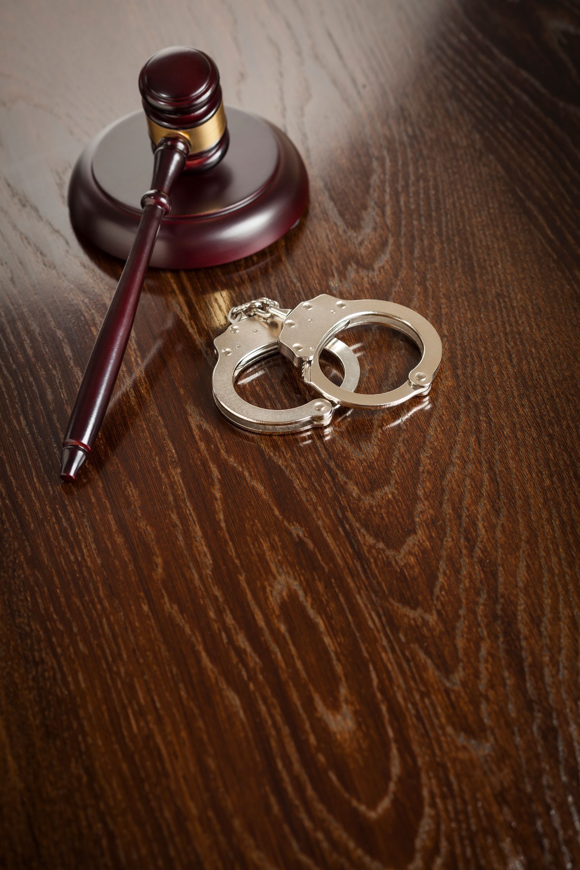 Gavel and handcuffs on a wooden surface, symbolic of law and justice.