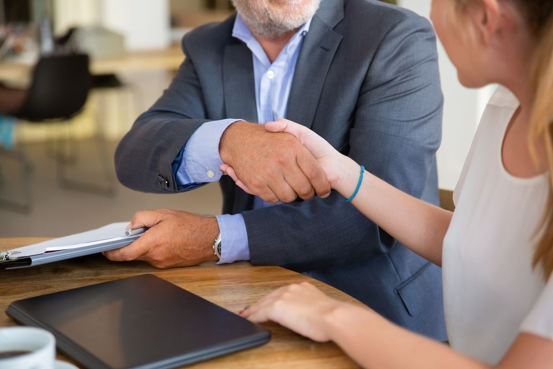 Man in a suit shaking hands with a woman at a table, likely in an office setting.