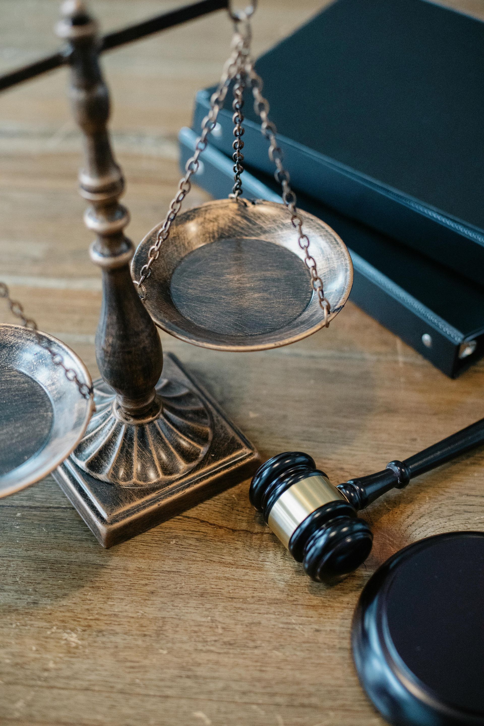Scales of justice and a gavel on a wooden desk with a stack of books in the background.