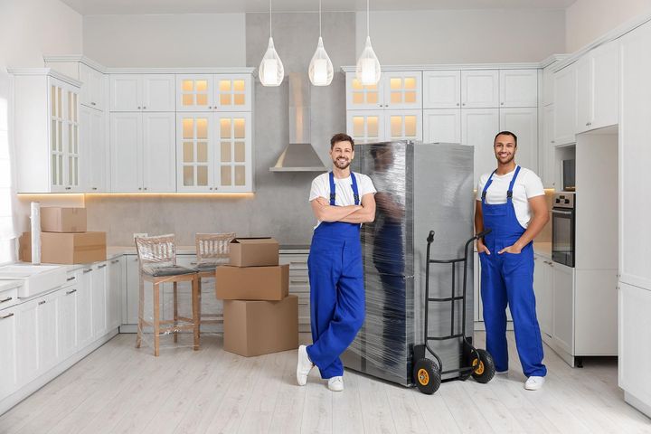 two men are standing in a kitchen next to a refrigerator .