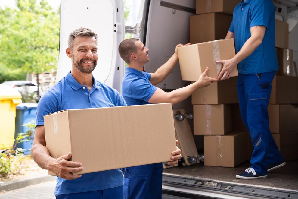 three men are loading boxes into a moving van .