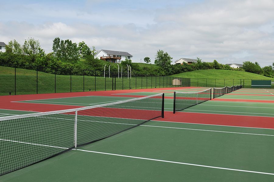 A tennis court with a fence and houses in the background