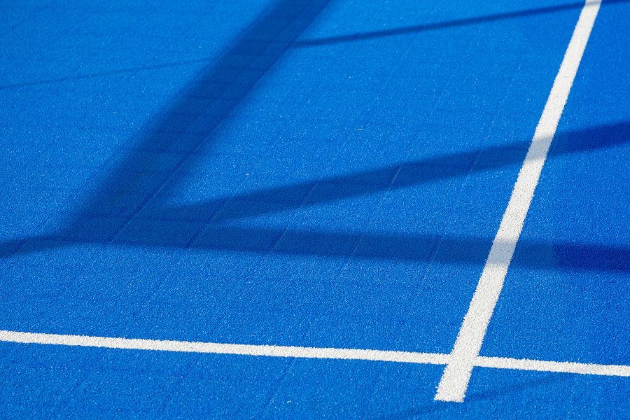 A blue tennis court with white lines and shadows