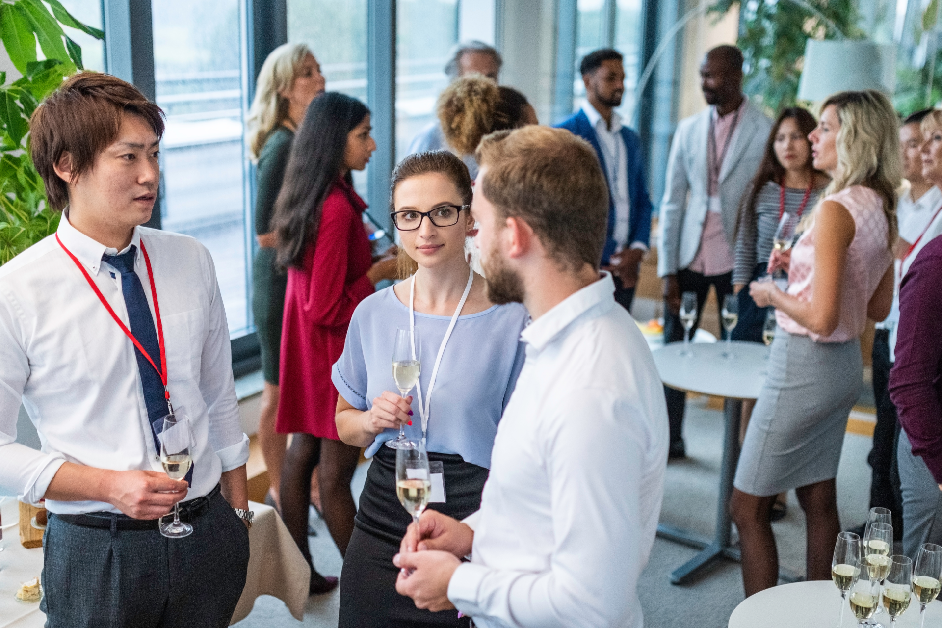 People network at a brightly lit indoor conference, holding glasses and conversing in a modern, open office space.