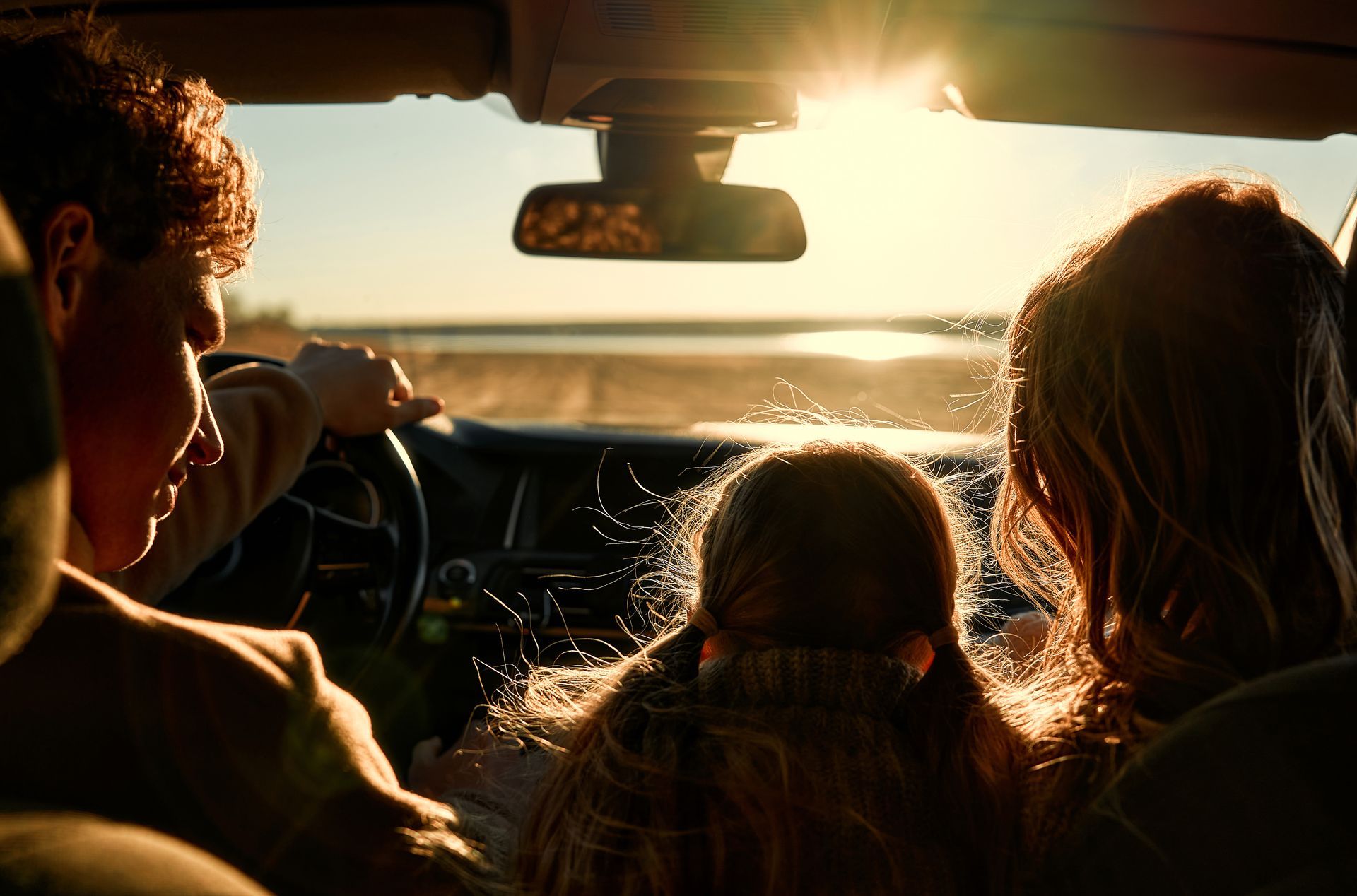 A family inside a car at sunset, silhouetted against the bright horizon through the windshield.