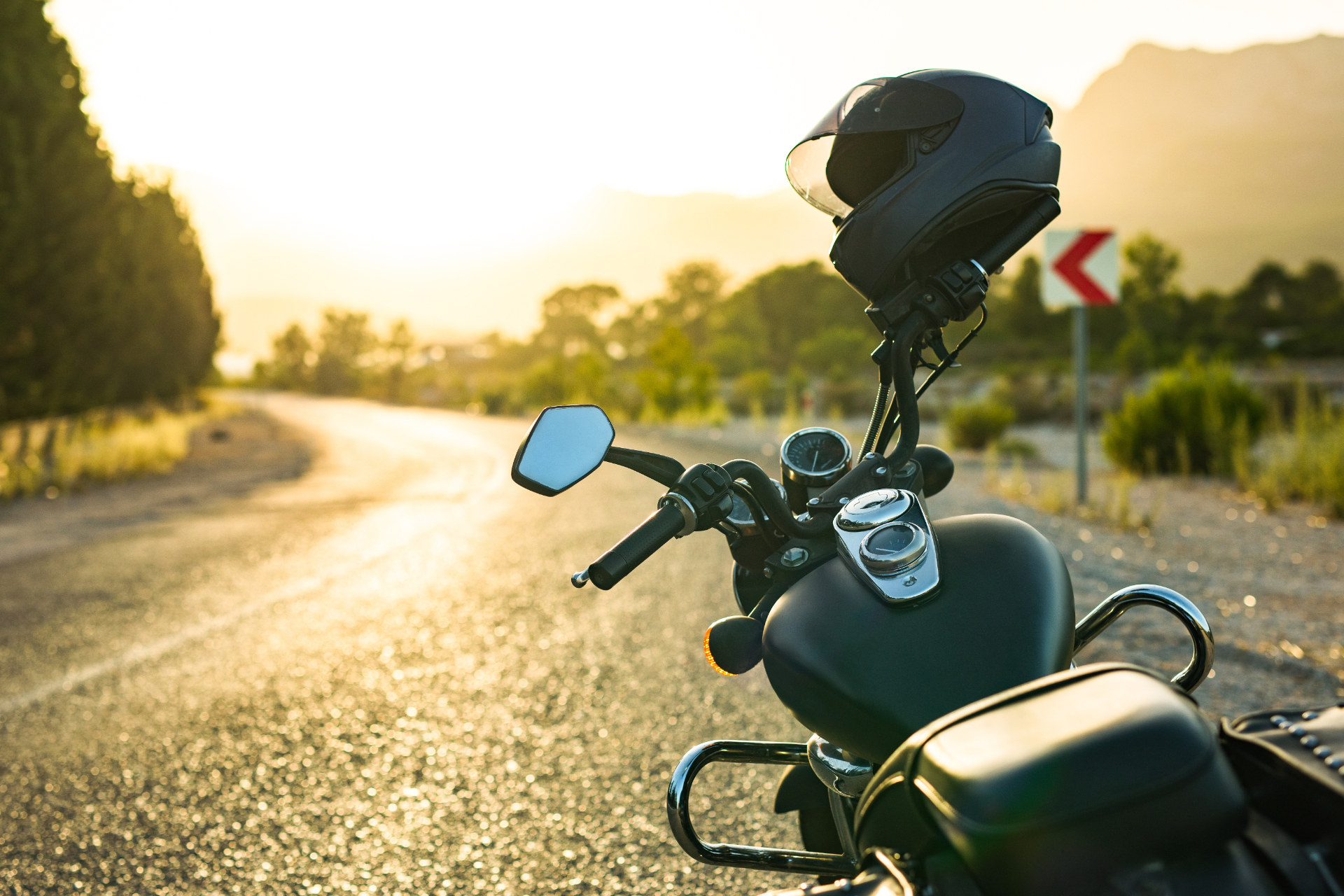 A black motorcycle parked on the side of a sunlit road with a helmet resting on the handlebars.