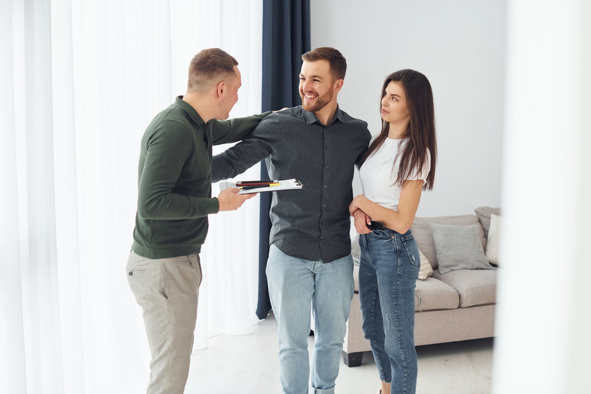 A real estate agent presents documents to a couple inside a bright, modern room.