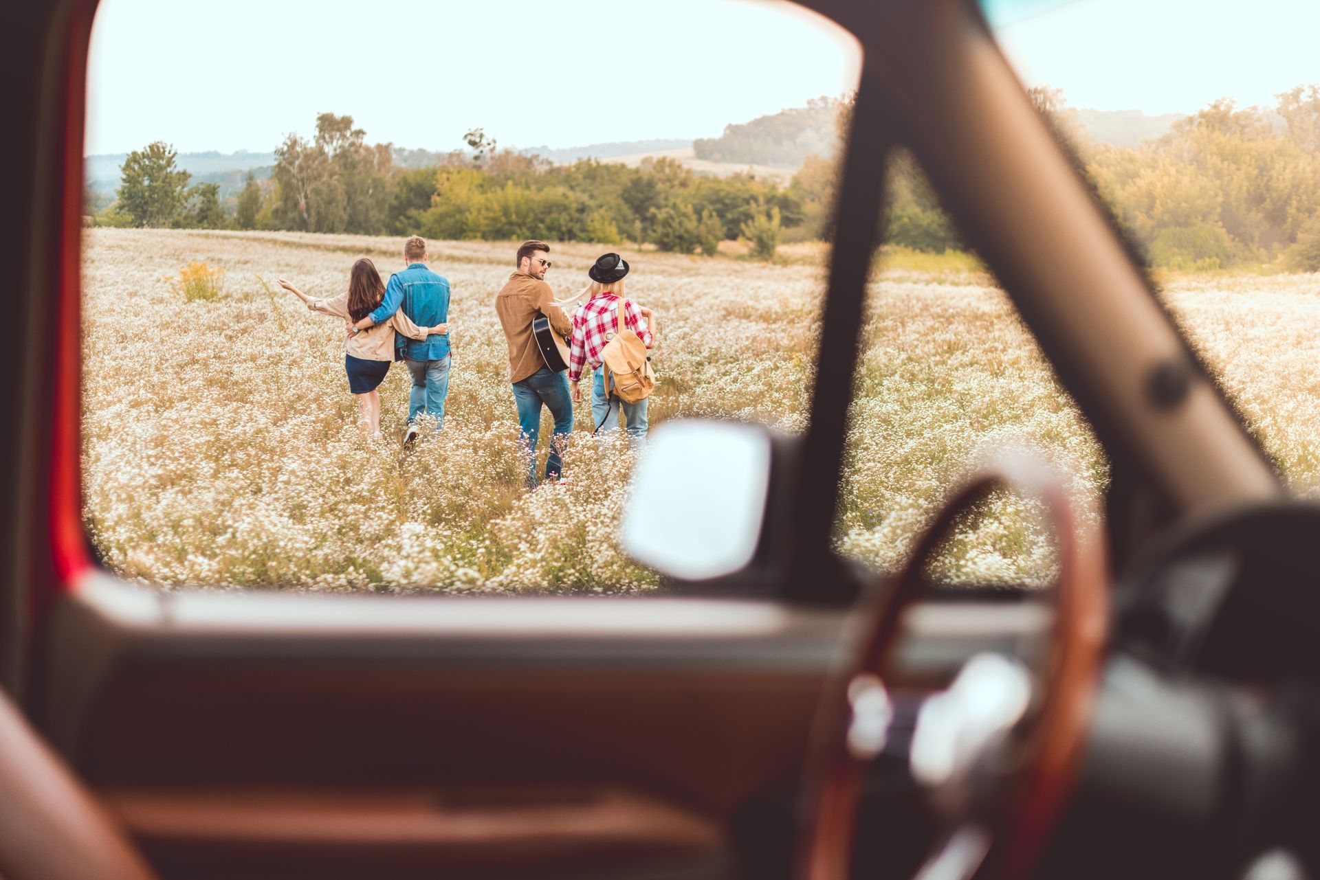 A view from a car window showing four people walking through a sunny, golden field.