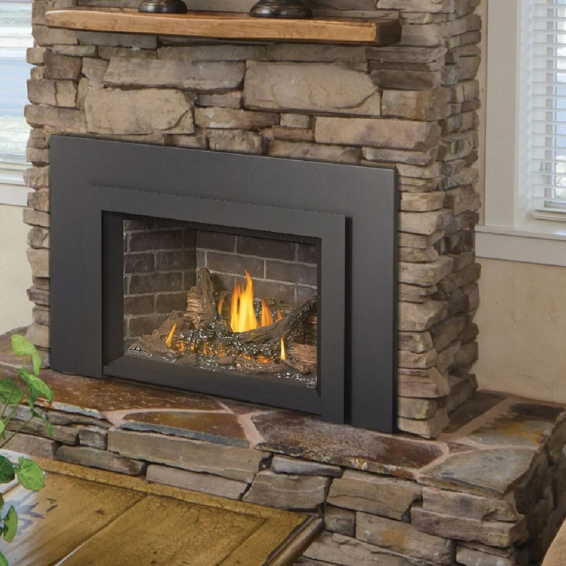 Fireplace with stone surround, black frame, and burning flames.