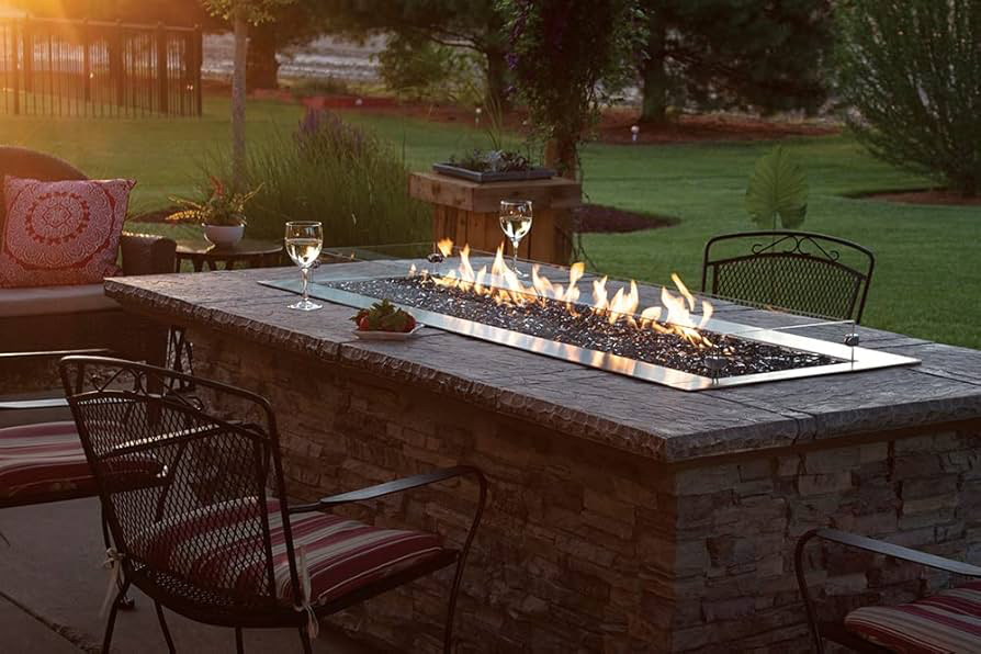 Outdoor fire pit with flames, drinks, and seating on a patio at dusk.