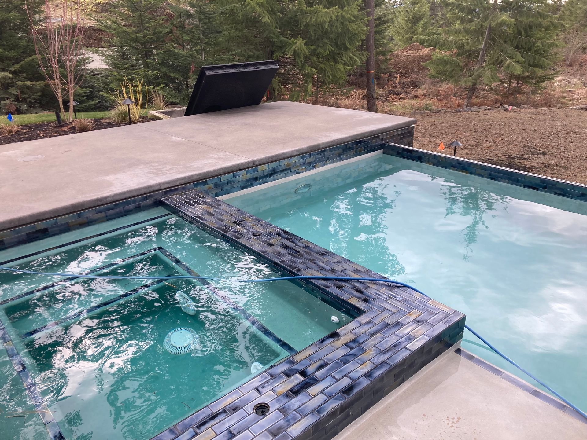 Pool and spa with blue tile trim; concrete deck. Jacuzzi jets create bubbles.