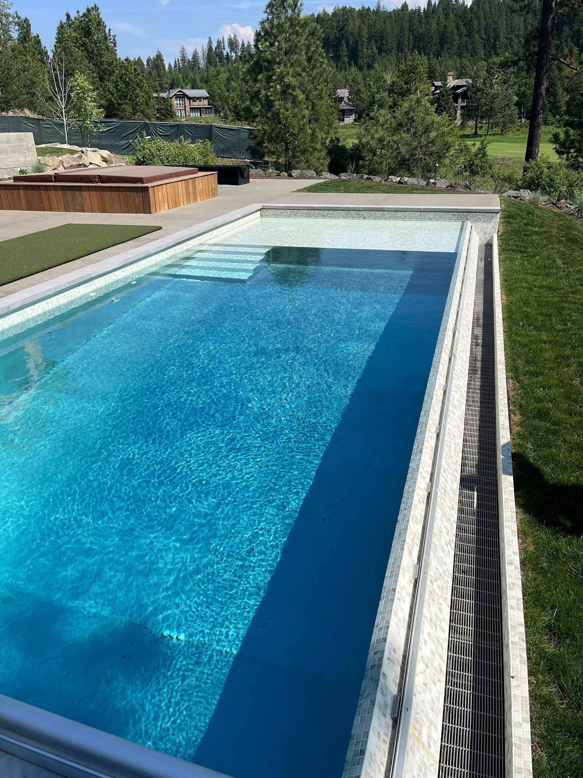 Swimming pool with blue water and stone surround, built-in steps, and green grass.