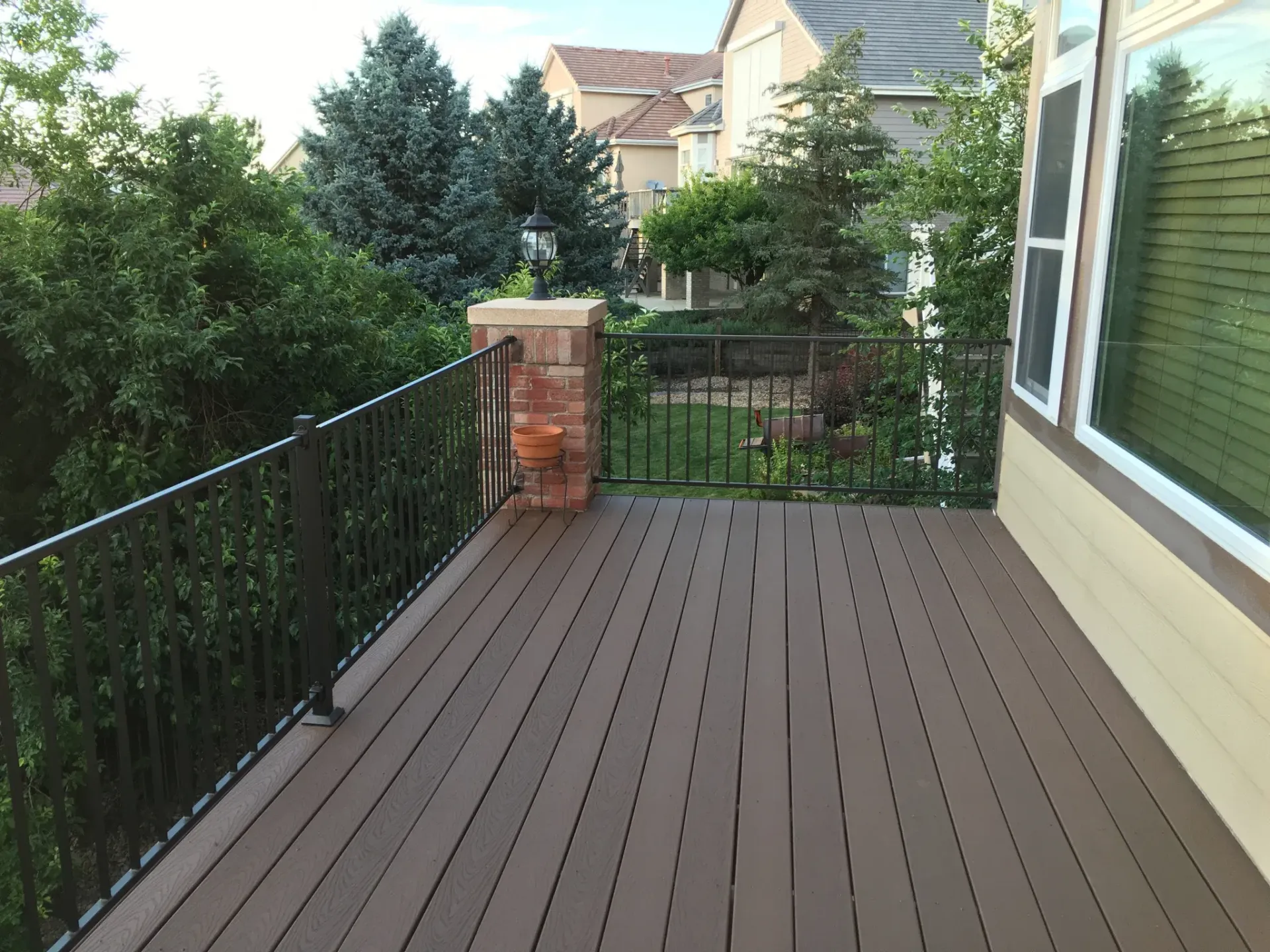 Wooden deck with black railing, overlooking a yard with trees and houses.