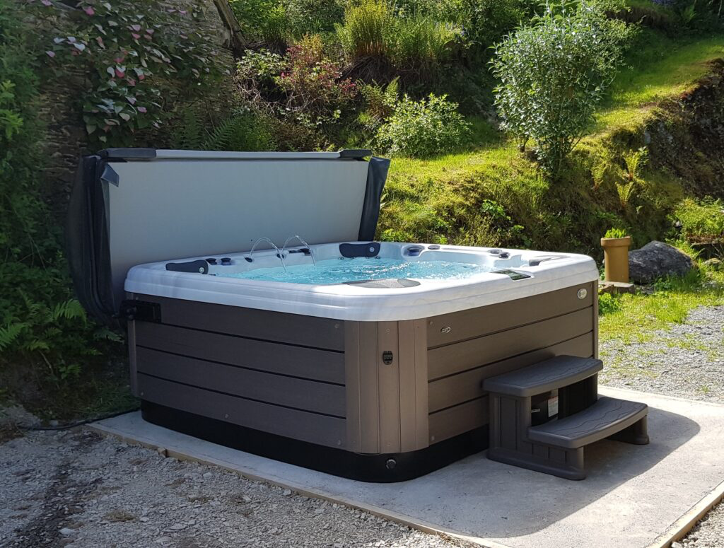 Hot tub with cover open, set on a concrete pad with steps, in a grassy outdoor setting.