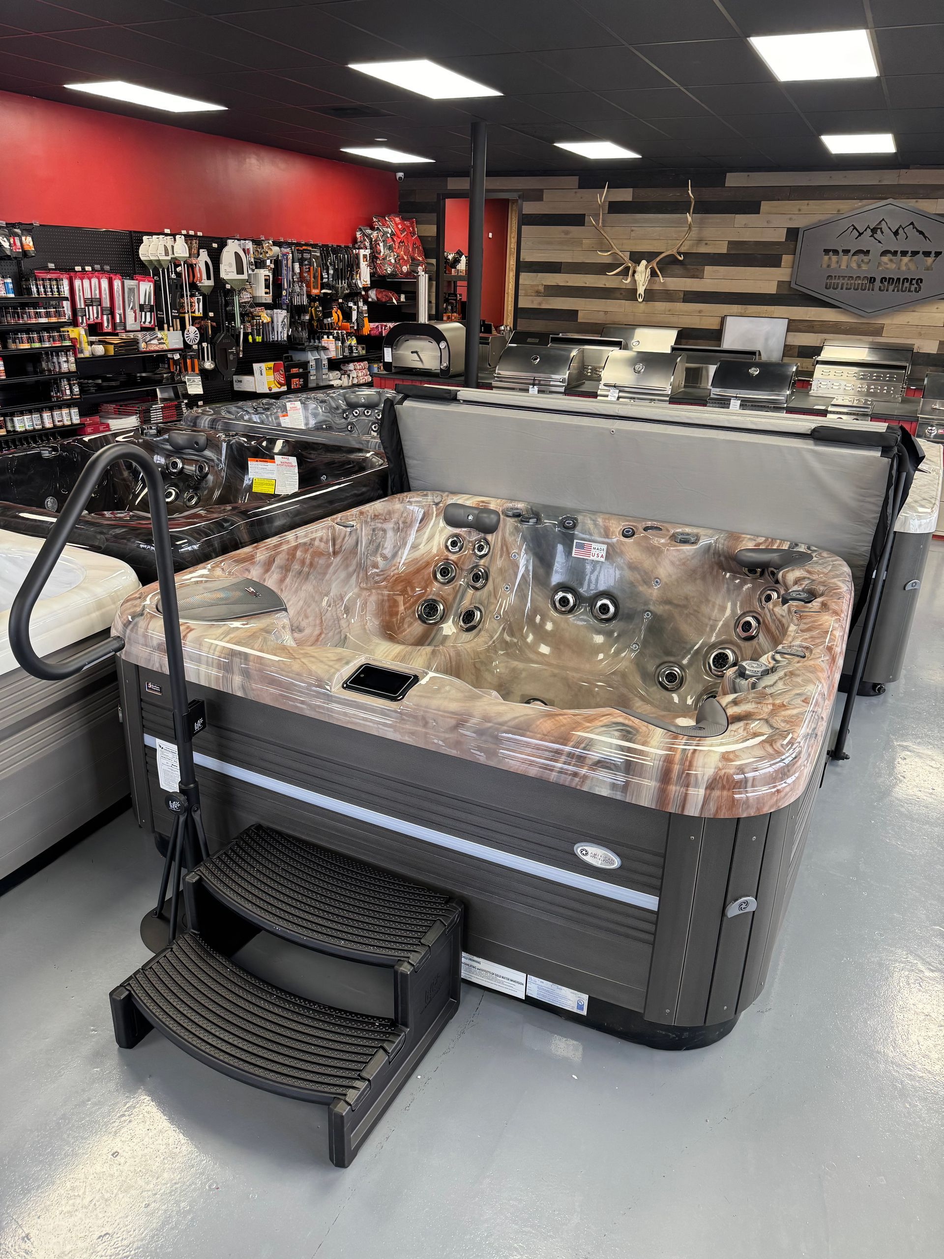 Hot tub on display in a store, dark gray exterior, brown and tan speckled interior, steps for entry.