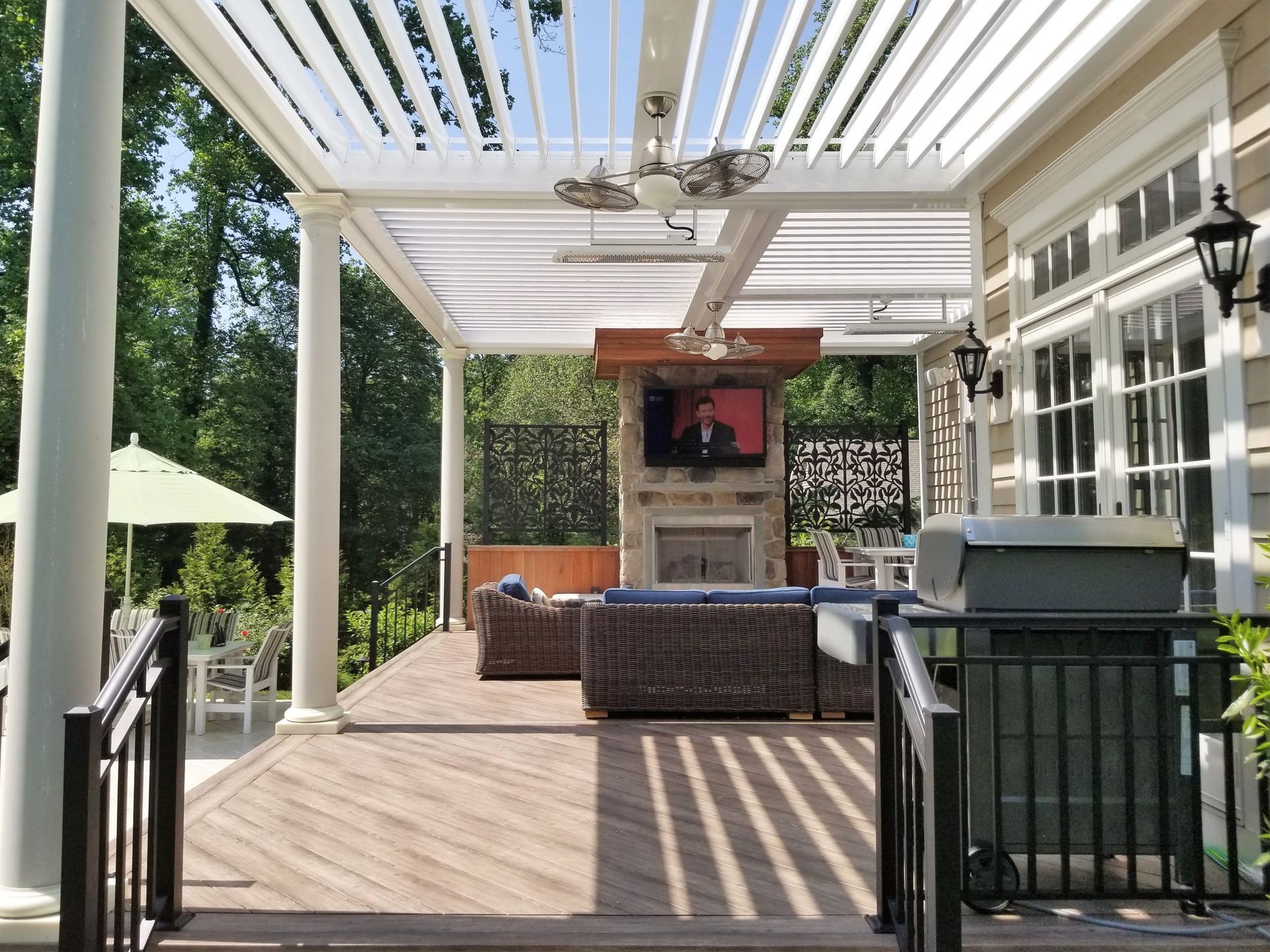 Outdoor patio with pergola, fireplace, and seating area. Wooden deck with grill and railing.