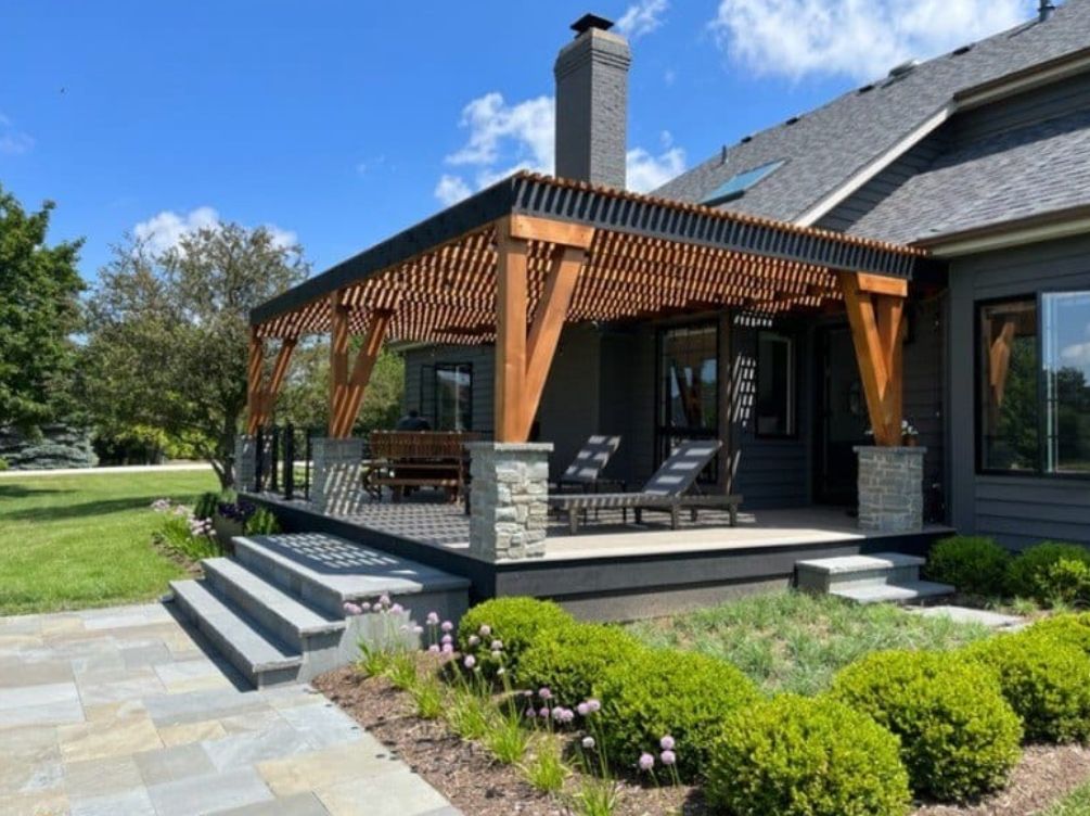 Wooden pergola over a gray deck with a stone staircase and green lawn.