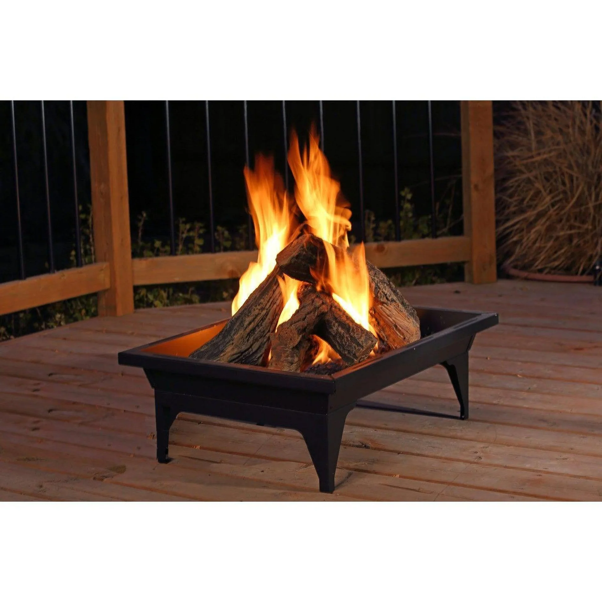 Fire pit with burning logs on a wooden deck at night.