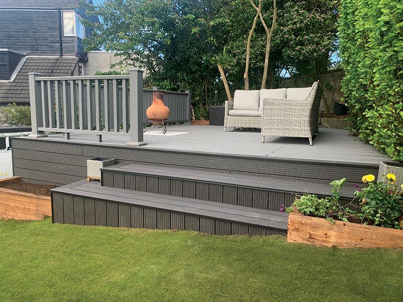 Multi-level gray composite deck with seating area and steps, surrounded by green lawn and plants.