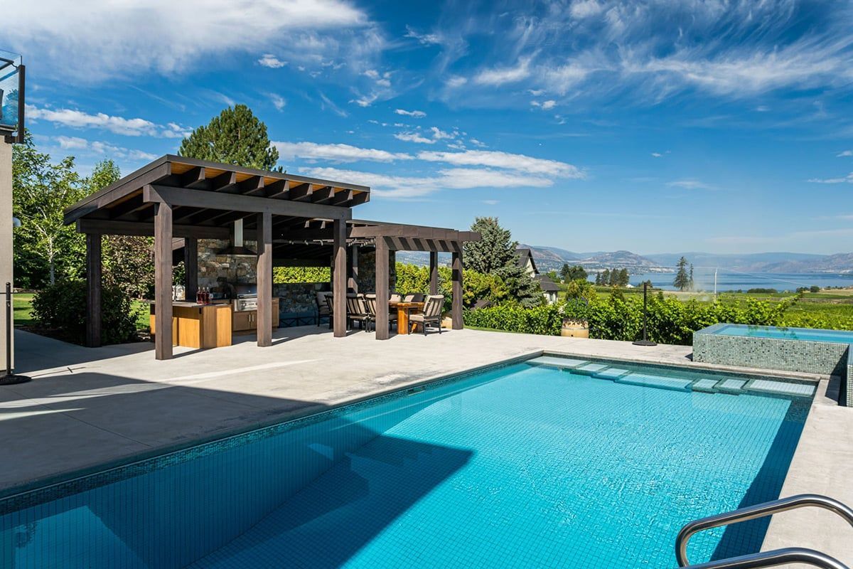Swimming pool with a pergola and scenic view under a blue sky.