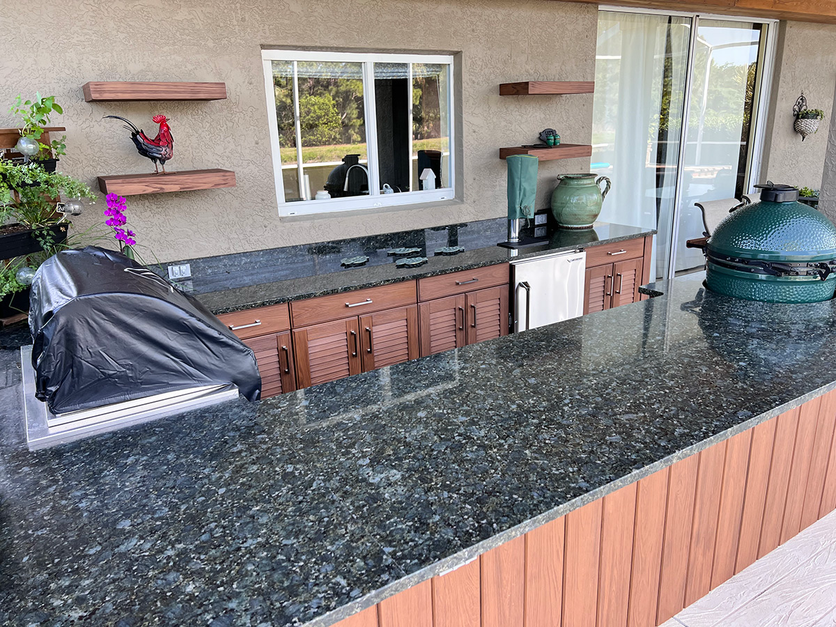 Outdoor kitchen with granite countertop, cabinets, grill, Big Green Egg, and shelves.