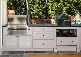 Outdoor kitchen with stainless steel grill, Big Green Egg, and white cabinets.